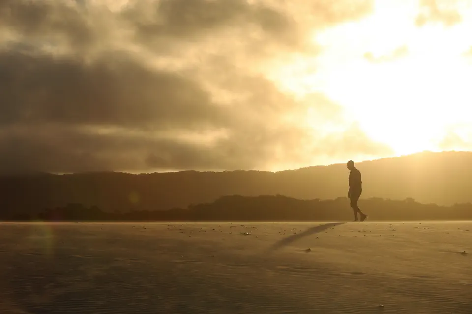 A small figure walking across a wide beach into hazy golden light