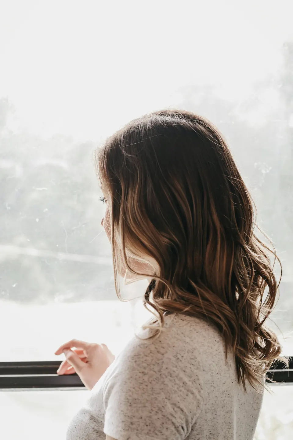 A woman by a bright window, face turned away, in soft morning light