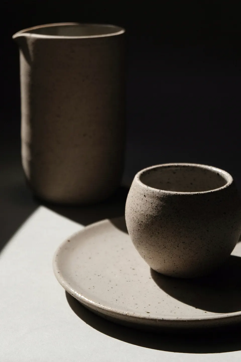 A stoneware cup and pitcher in hard morning sun with deep shadows