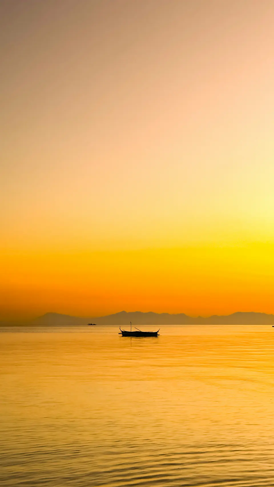 A lone boat on a gold sea under an orange sunset sky