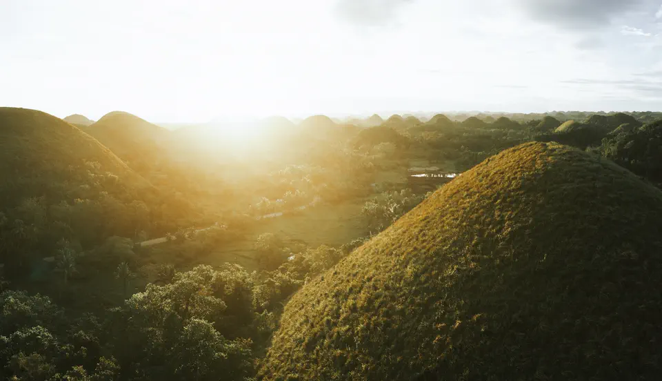 Rows of rounded green hills fading into sunrise haze
