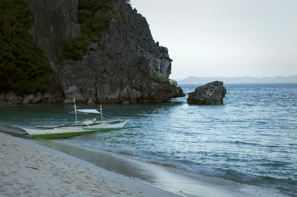 An outrigger boat moored below limestone cliffs on calm blue water