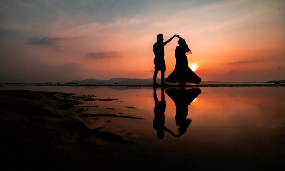 A couple dancing in silhouette at sunset, mirrored in the wet sand