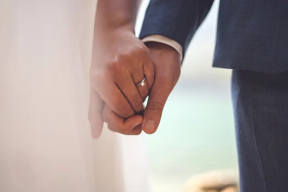 The couple's hands, a ring catching the light, the sea blurred behind