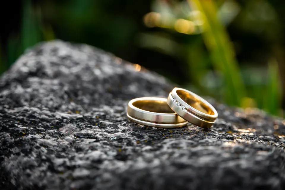 Two gold wedding bands resting on dark stone in warm light