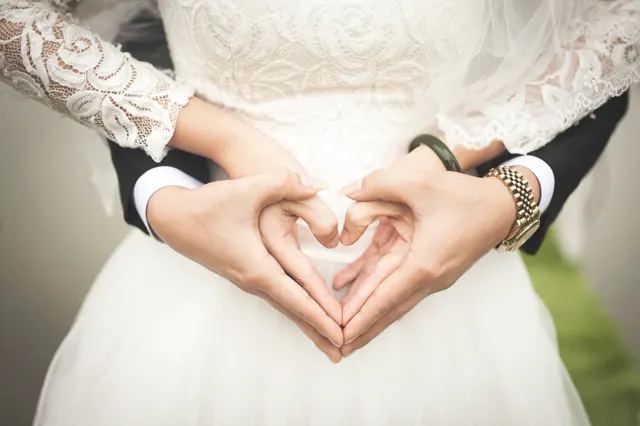 A couple making a heart shape with their hands against a lace wedding dress
