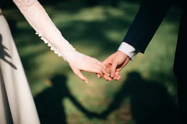 Two hands joined, with the couple's shadows holding hands on the grass below