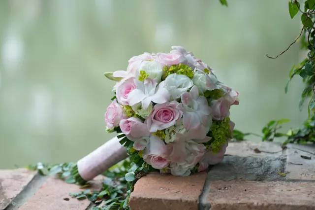 A round bouquet of pink and white roses resting on a garden brick wall