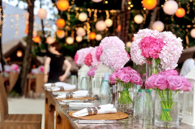 A long reception table with pink hydrangeas and warm paper lanterns overhead
