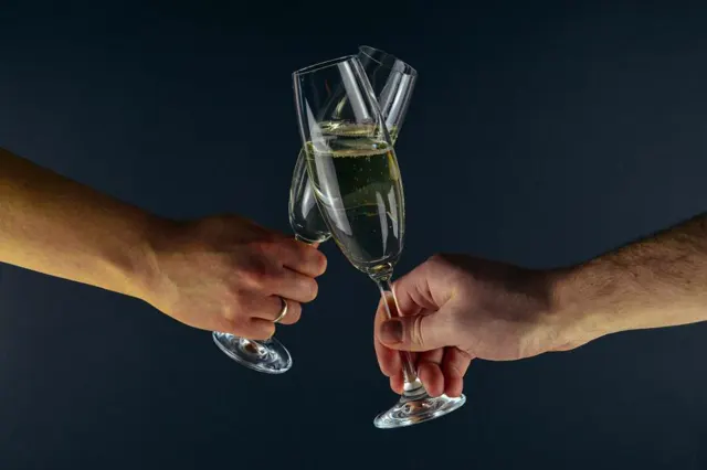 Two hands clinking champagne glasses against a dark background