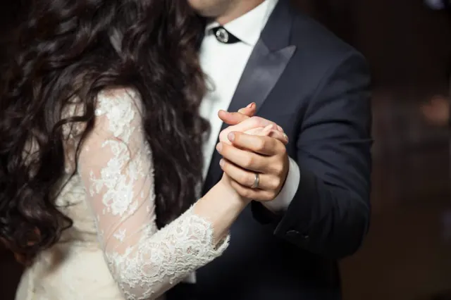 A couple dancing close, her lace sleeve resting in his hand