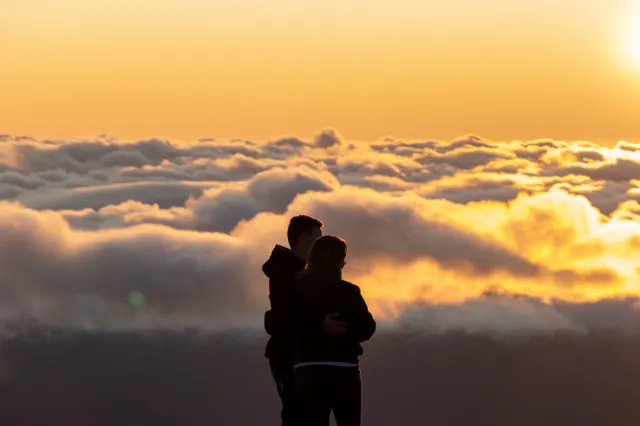 A couple silhouetted above a sea of clouds at sunrise
